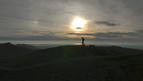 lone mountain walker silhouetted by golden hour low sun crossing high fell summit