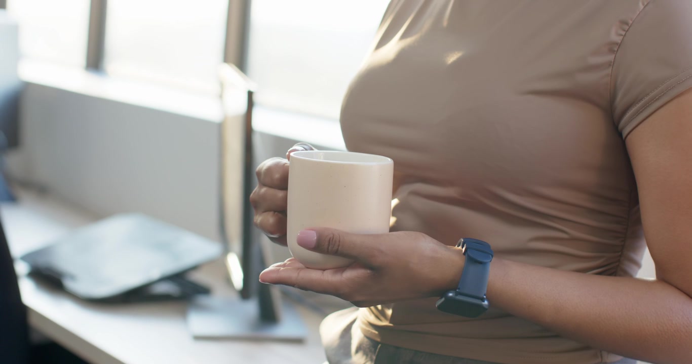 Mulher segura e ajusta a pegada de uma caneca de cerâmica, fazendo uma pausa na mesa perto da janela