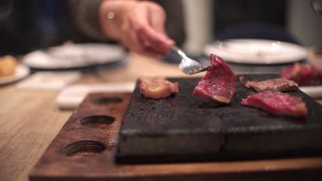 friends eating at restaurant celebrating birthday in dinning room, toasts, cheers and preparing their own meat at hot stone