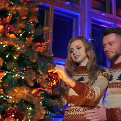 young family decorates christmas tree. cheerful girl is hanging christmas ball. couple in love prepare house for new year holidays. view from below.