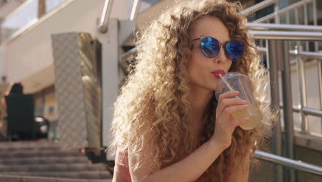 woman with curly hair drinking smoothie outdoors