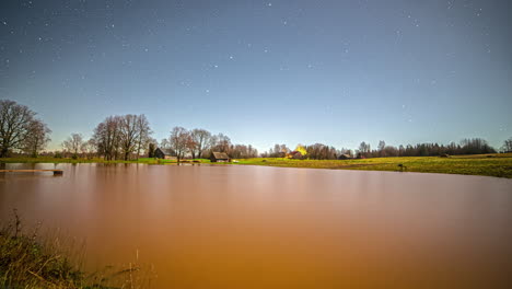 a bright moon and star-filled sky over a cabin by the lake - wide angle time lapse