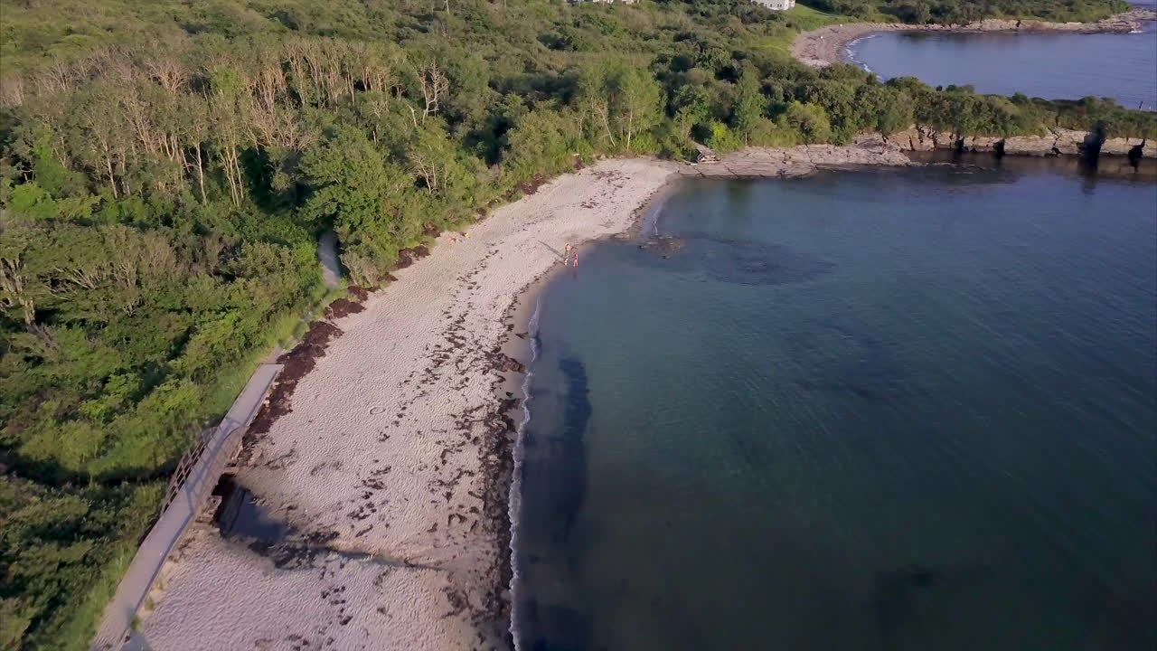 푸른 대서양과 메인 해안선의 무성한 녹색 숲 사이의 하얀 모래 해변 위로 날아가는 공중 샷