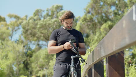 Front-view-of-serious-athlete-using-phone-during-cycling-in-park