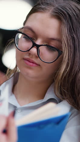 la dama con gafas abre cuidadosamente una nueva página, la cabeza inclinada hacia un lado, centrada en la lectura, tres grandes luces brillan en el fondo borroso, creando un ambiente cálido y moderno