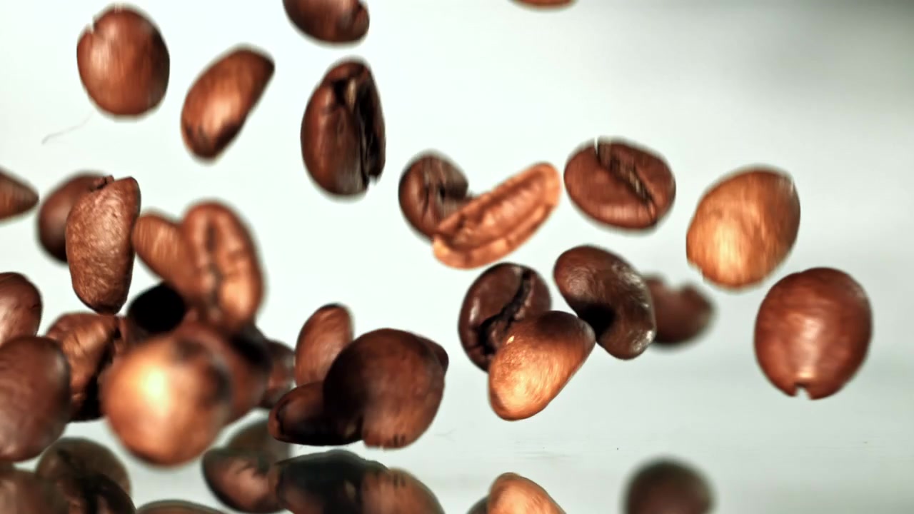 Chicchi di caffè tostati che cadono al rallentatore su sfondo bianco