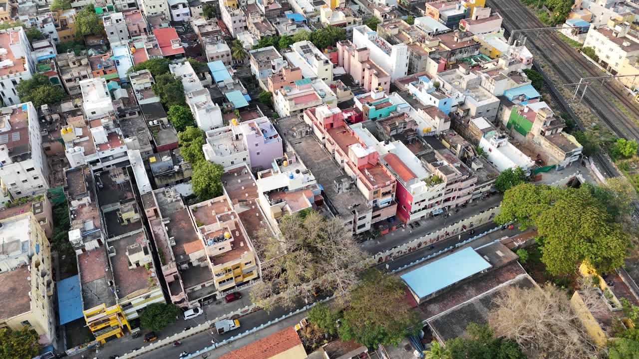 Aweial view of Chennai. The frame is filled with tightly packed residential buildings and colorful rooftops, contrasted by the parallel lines of a major railway cutting through the urban landscape