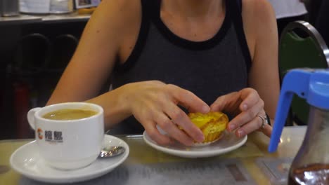 turista mujer mordiendo tarta de huevo en un café en hong kong