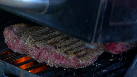 two thick and juicy rib eye steaks are covered as a grills lid is closed in slow motion