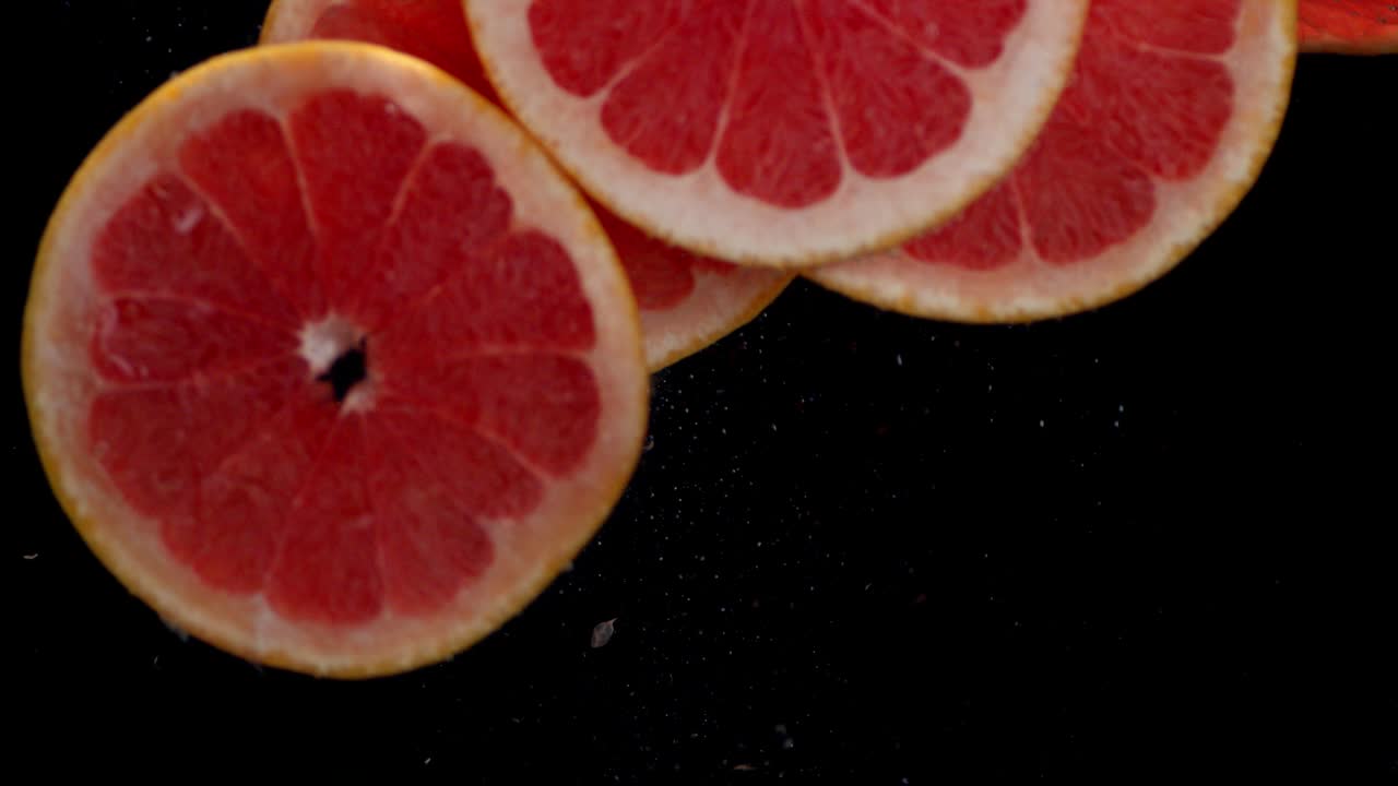 Round slices of ripe grapefruit fall into the water with air bubbles.