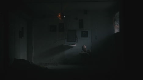 pale bald skinny man sits next to the wall in the creepy old bathroom at night