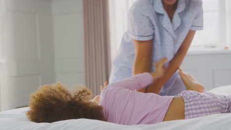 familia con dos madres con pijama jugando en la cama en casa con su hija