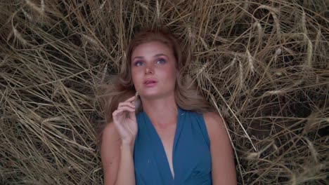 Attractive-young-woman-lying-in-the-golden-wheat-field.-Her-hand-is-touching-wheat-ear.-Harvest-concept.-Harvesting.-Slow