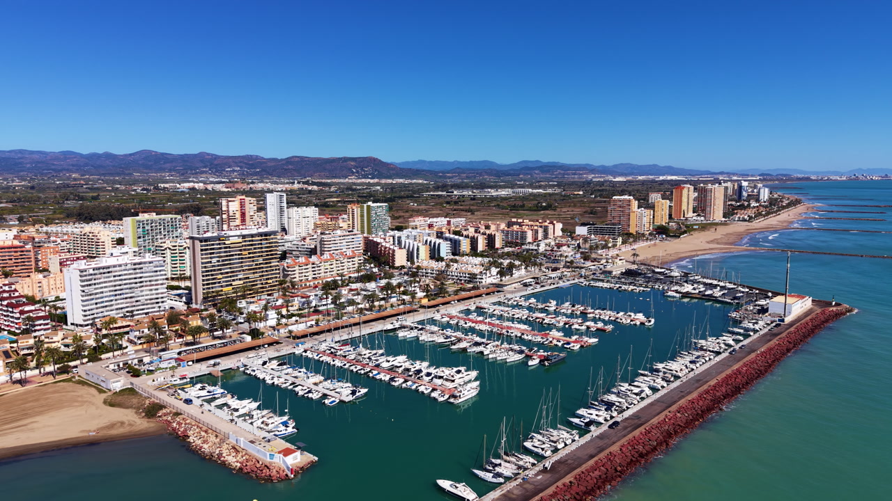 Pobla de Farnals marina and coastal town in Valencia, Spain, with sailboats docked, sandy beach, apartments, and mountain backdrop