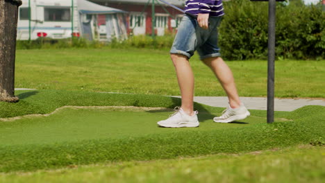 Junger-Mann-In-Shorts-Wartet-Und-Analysiert-Den-Platz,-Bevor-Er-Den-Minigolfball-Trifft-Und-Minigolf-Auf-Dem-Campingplatz-Spielt,-Der-Spaß-Hat-Sommerspiele-Partyaktivität-Freunde-Im-Golfcluburlaub-Mit-Eis