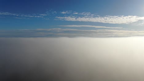 drone rises over a foggy landscape on a beautiful blue sky day with mottled clouds to reveal a mountain vista