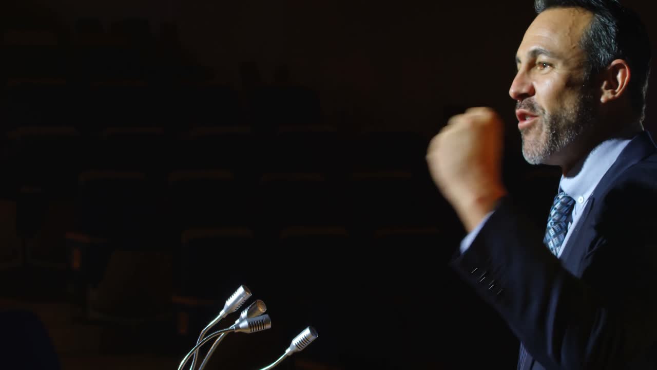 Caucasian businessman speaking at podium on stage in auditorium 4k