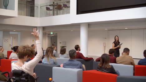 Teacher-presenting-to-a-university-class,-some-raising-hands