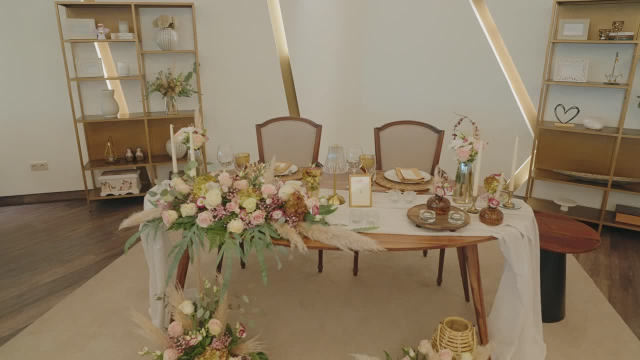 Mesa nupcial para los novios con camino de mesa floral rosa dentro de una tienda tipi dorada con decoración de estantes.