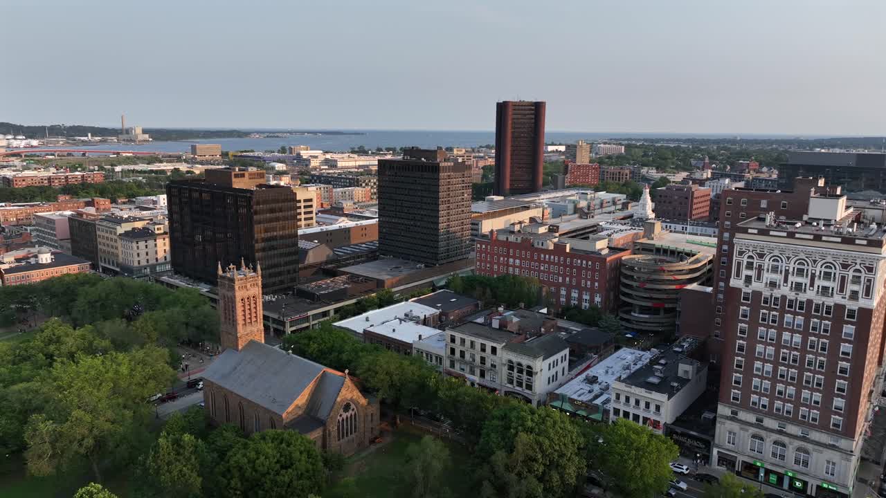 Trinity on the Green Episcopal Church with Wells Fargo bank building near park in downtown New Haven. Aerial wide shot. Long Island sound and coast in background. Sunset time in Connecticut