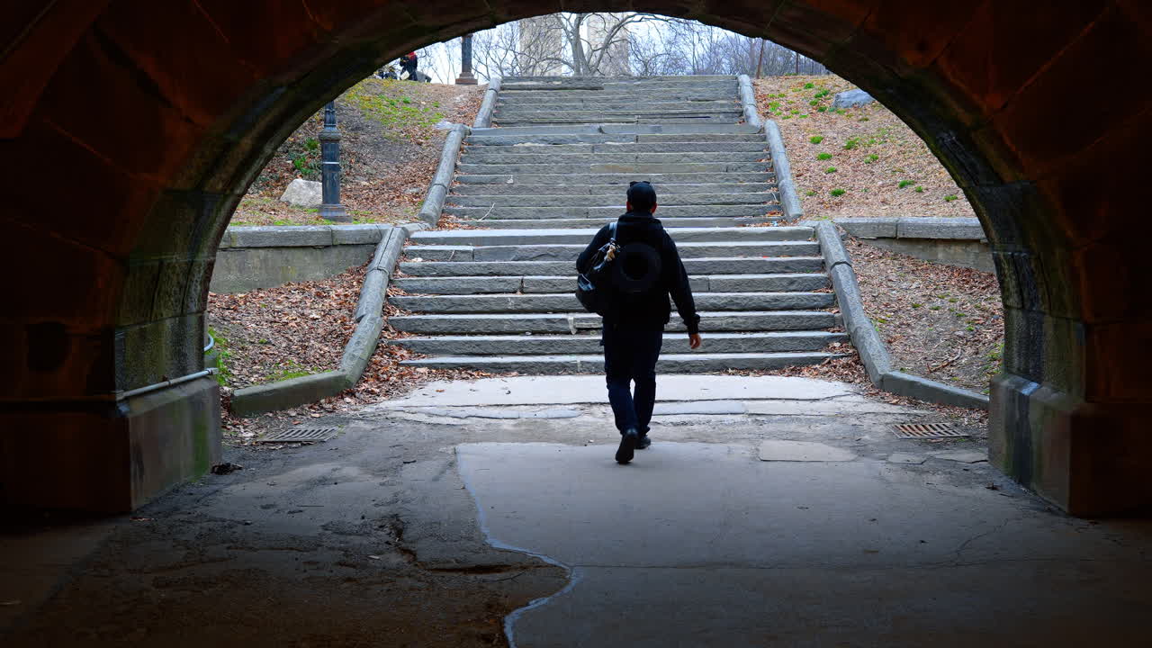 New York, USA, 14 March 2026: Silhouette of person walking through stone arch tunnel. Dark silhouette of a man walking through a stone tunnel towards bright outdoor stairs in a public park