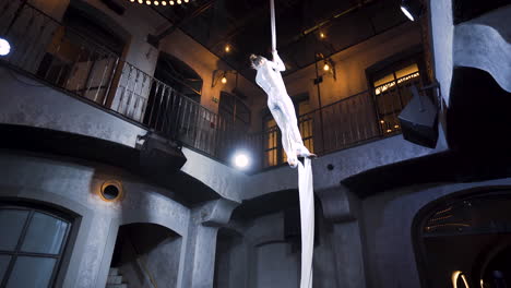 female aerial acrobat doing a midair split on silks in a club venue