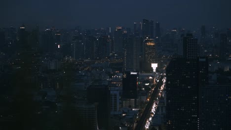 Bangkok-night-skyline-with-busy-road-and-blurry-bush-foreground