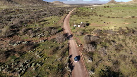 Aerial-shot-of-car-on-dirt-road-in-Willcox,-Arizona,-wide-rotating-drone-shot-with-mountains-in-the-background