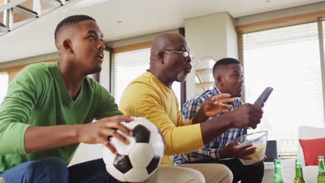 African-american-father-and-twin-teenage-sons-sitting-on-couch-watching-game-on-tv-and-talking