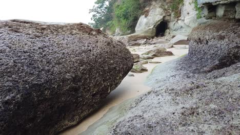 the rocks on the beach at low tide are large boulders from ancient volcanic eruptions with a mysterious cave in the background