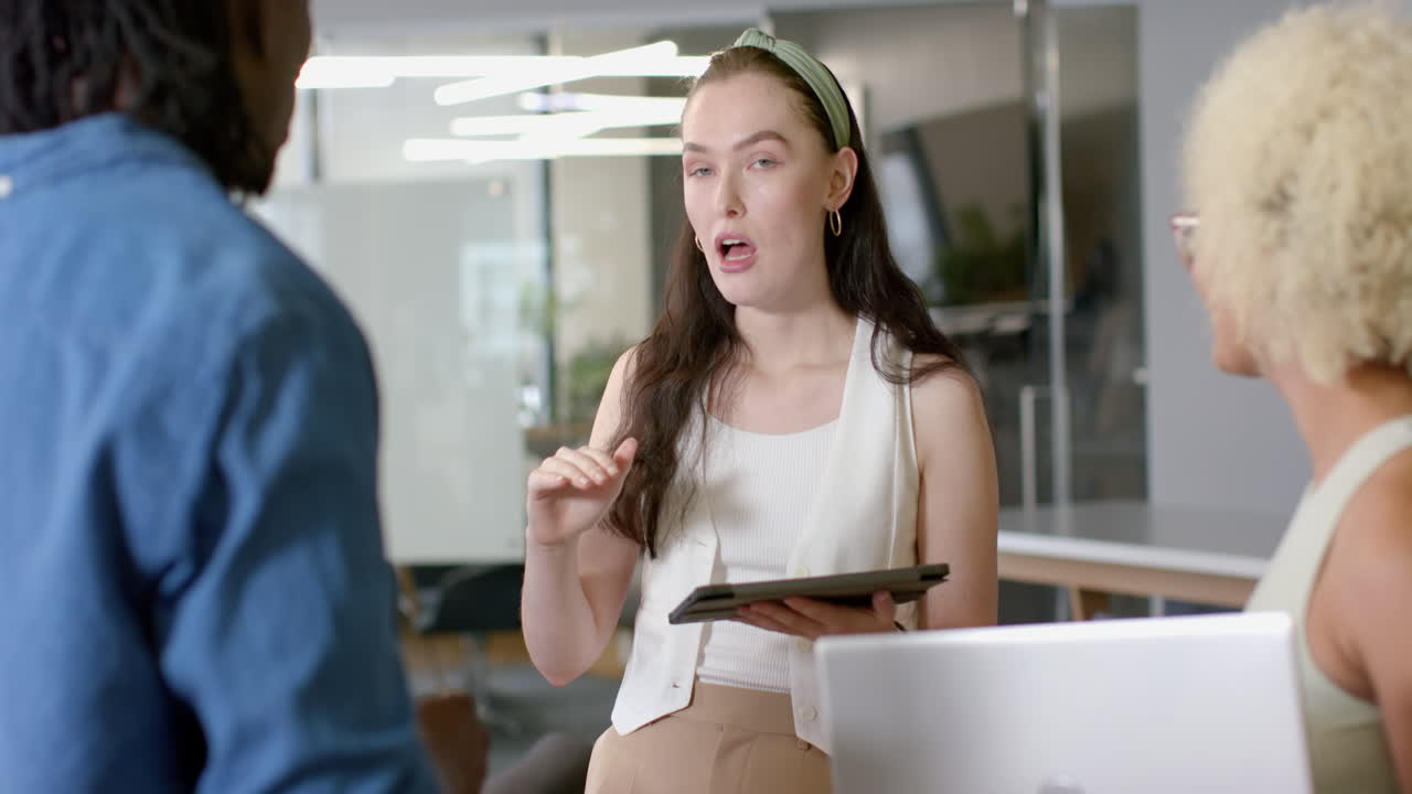 Discussing project, woman holding tablet talking to colleagues in modern office