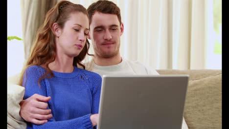 pareja feliz sentada en el sofá usando la computadora portátil