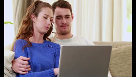 happy couple sitting on the couch using the laptop