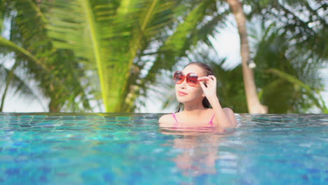 beautiful exotic woman sunbathing and relaxing in infinity swimming pool of caribbean resort hotel, slow motion