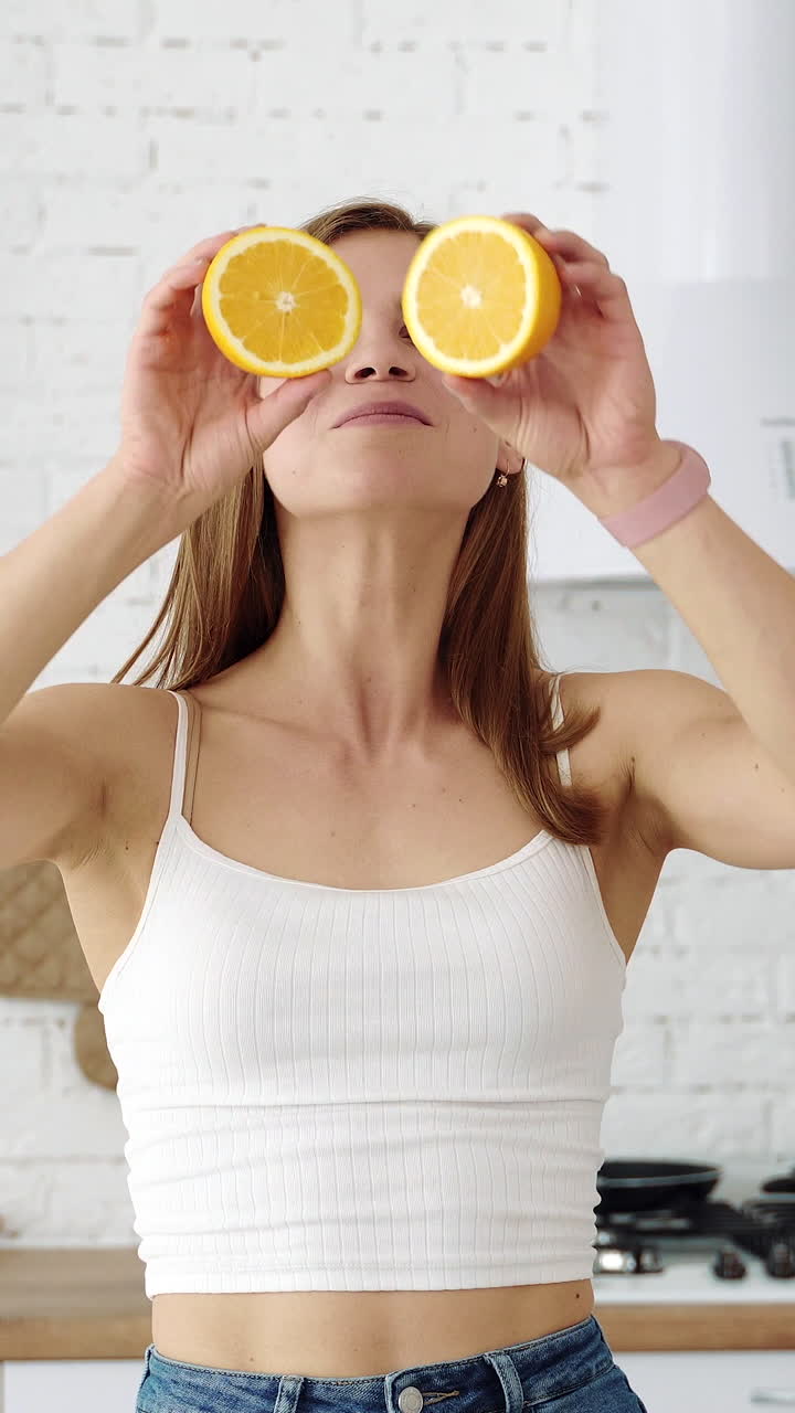 A positive smiling girl with orange slices in her hands closes her eyes. Vertical video