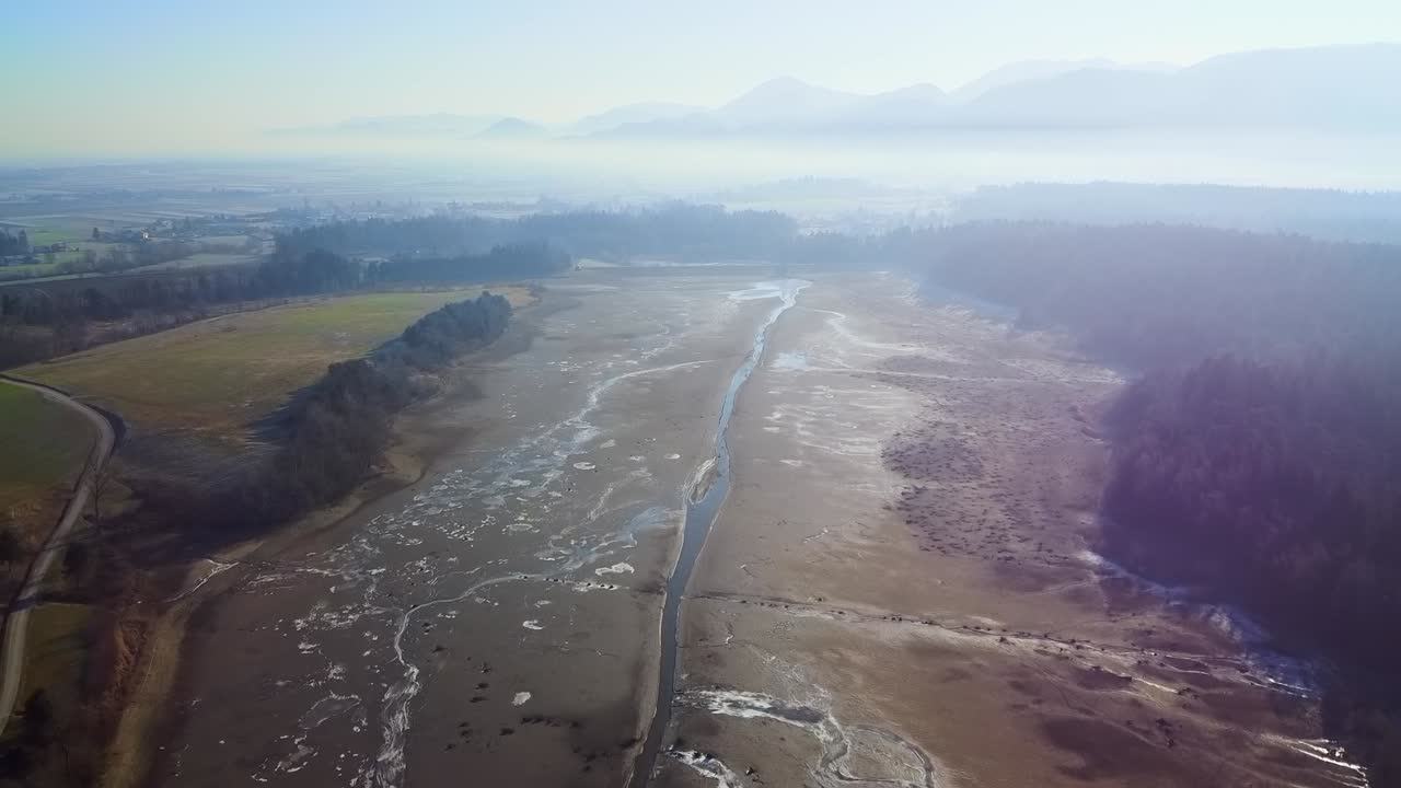 Mesmerizing endless view of nature showing a dried lake amidst beautiful greenery on a misty day. Aerial