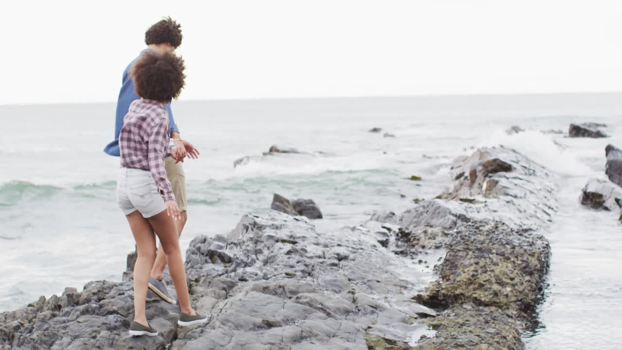 pareja afroamericana cogida de las manos caminando por las rocas cerca del mar