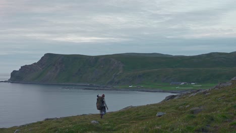 hiker treks down the riverbank with coastal cliff on the background in norway