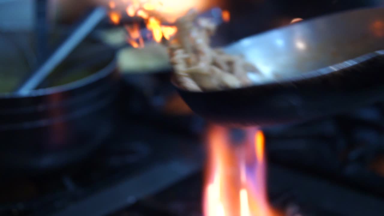 Pezzi di carne girati in padella su un fornello a gas con fiamme arancioni brillanti