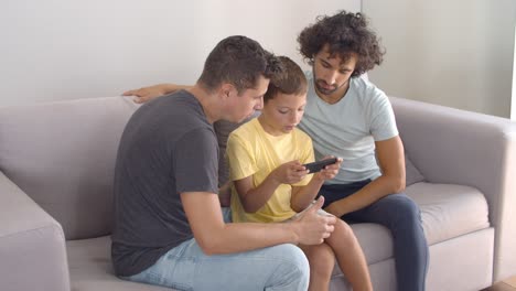 two dads helping son with online app on mobile phone