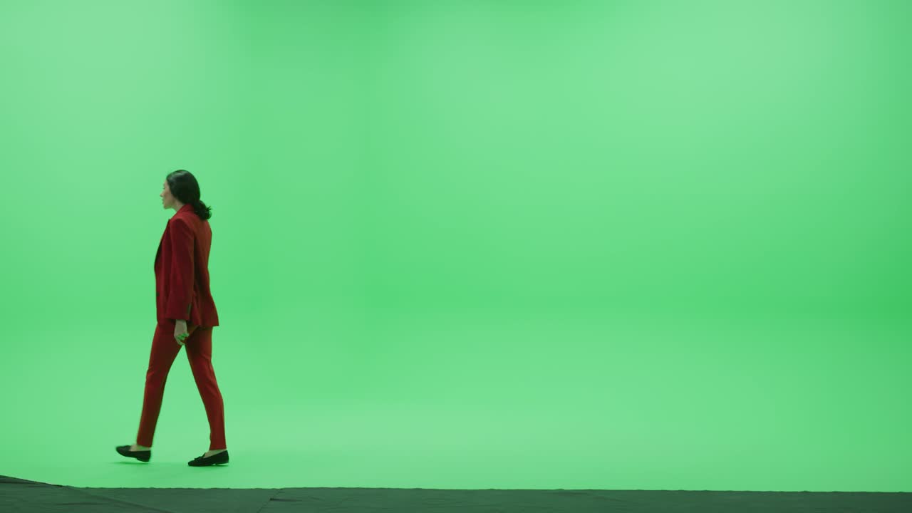 그린 스크린 크로마 키 스튜디오: 세련된 빨간색 슈트를 입은 아름다운 사업가 여성이 방을 오른쪽에서 왼쪽으로 고 있습니다.