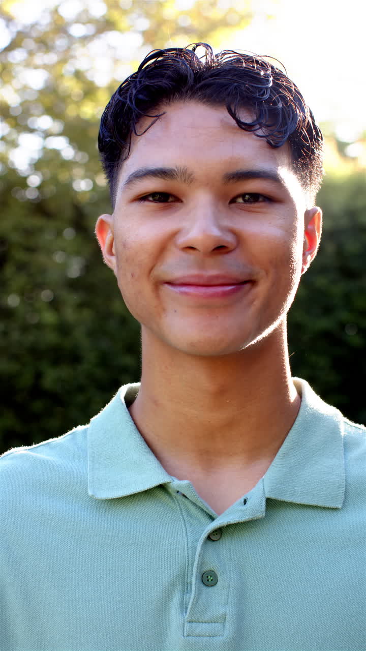 Vertical video: Smiling young man outdoors, wearing green shirt, enjoying sunny day