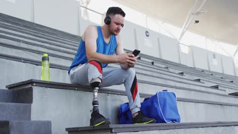 Atleta-Masculino-Caucásico-Discapacitado-Con-Pierna-Protésica-Sentado,-Usando-Auriculares