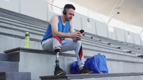atleta masculino caucásico discapacitado con pierna protésica sentado, con auriculares