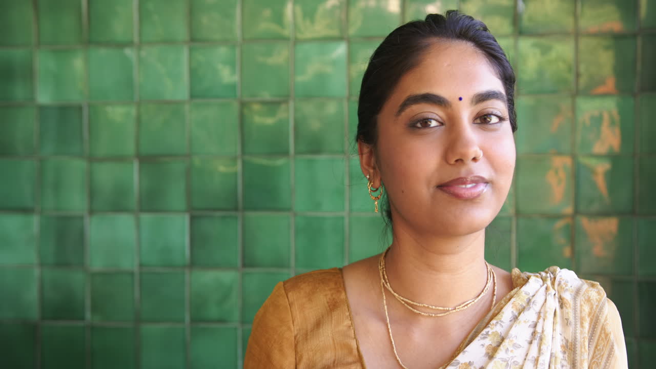 Smiling Indian woman in traditional sari posing against green tiled wall, copy space
