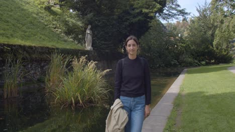 Chica-Posando-Frente-A-Una-Estatua-Antigua-A-Lo-Largo-De-La-Piscina-En-Stadt-Park-En-Graz,-Austria,-Plano-General