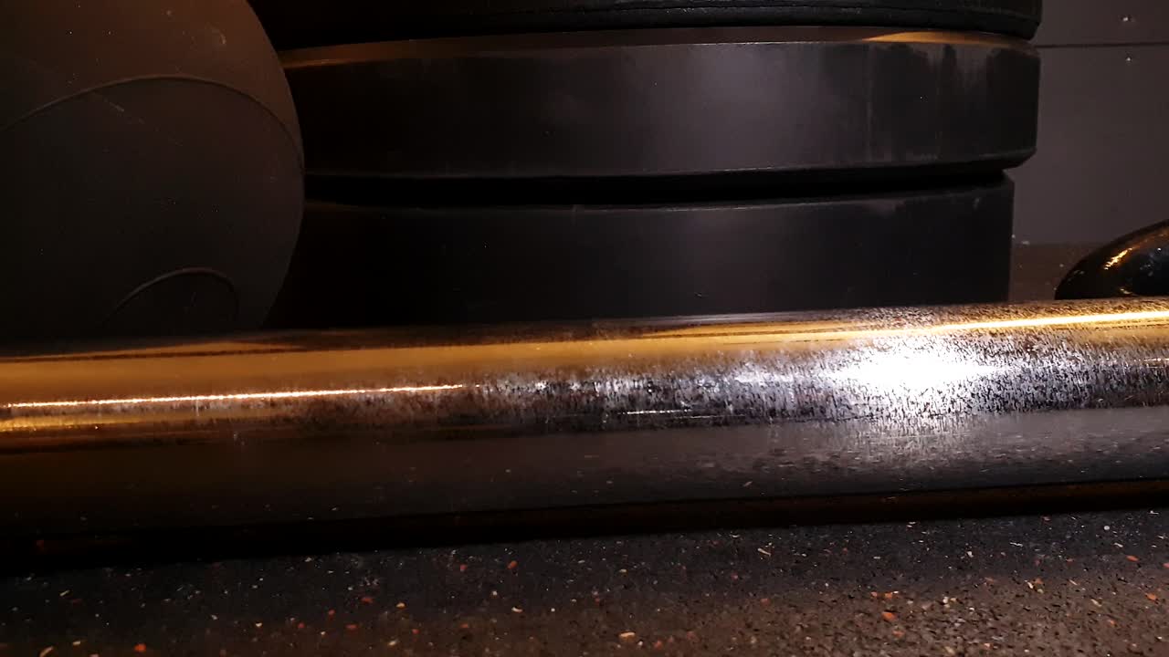 primer plano de la barra olímpica y una pila de placas de peso, gimnasio cerrando por la noche