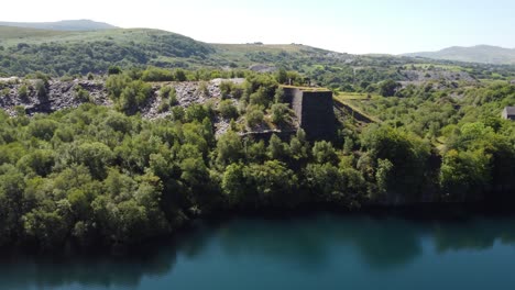 aerial view orbiting welsh woodland valley slate mining shaft and quarry lake revealing snowdonia mountains