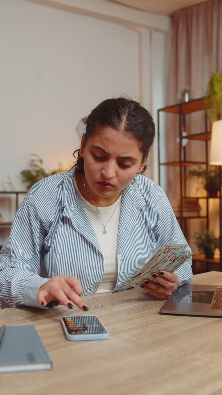 indio rico y independiente contando dinero en efectivo usando una aplicación de calculadora de teléfono inteligente en el escritorio de su casa