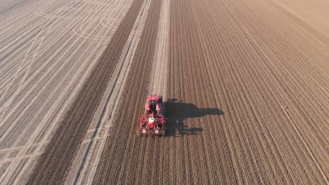 drone shot of red tractor plowing brown, earthy, dutch farmland